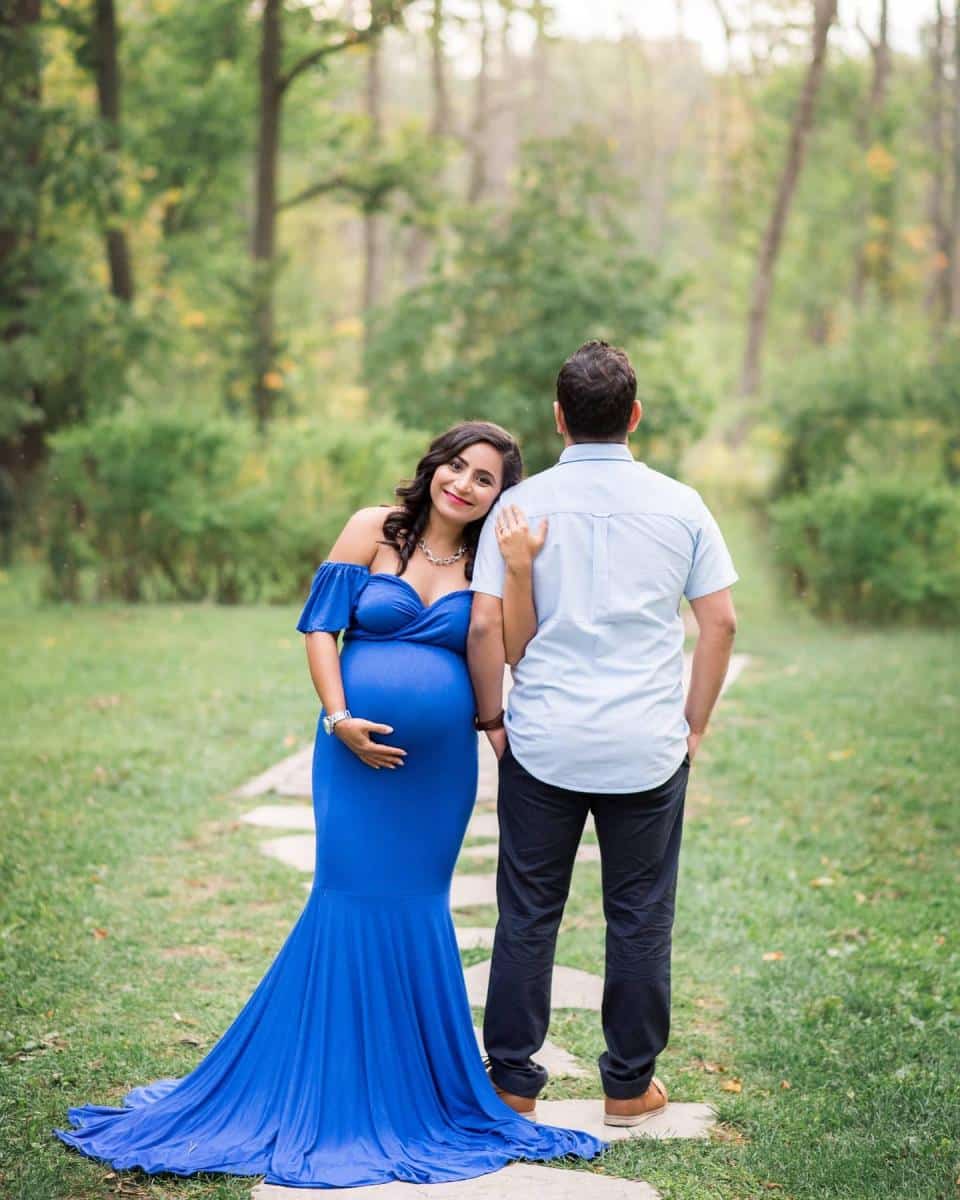 A pregnant woman in a stunning cobalt blue gown posing with her partner in a forest clearing for a maternity photo session Mississauga.