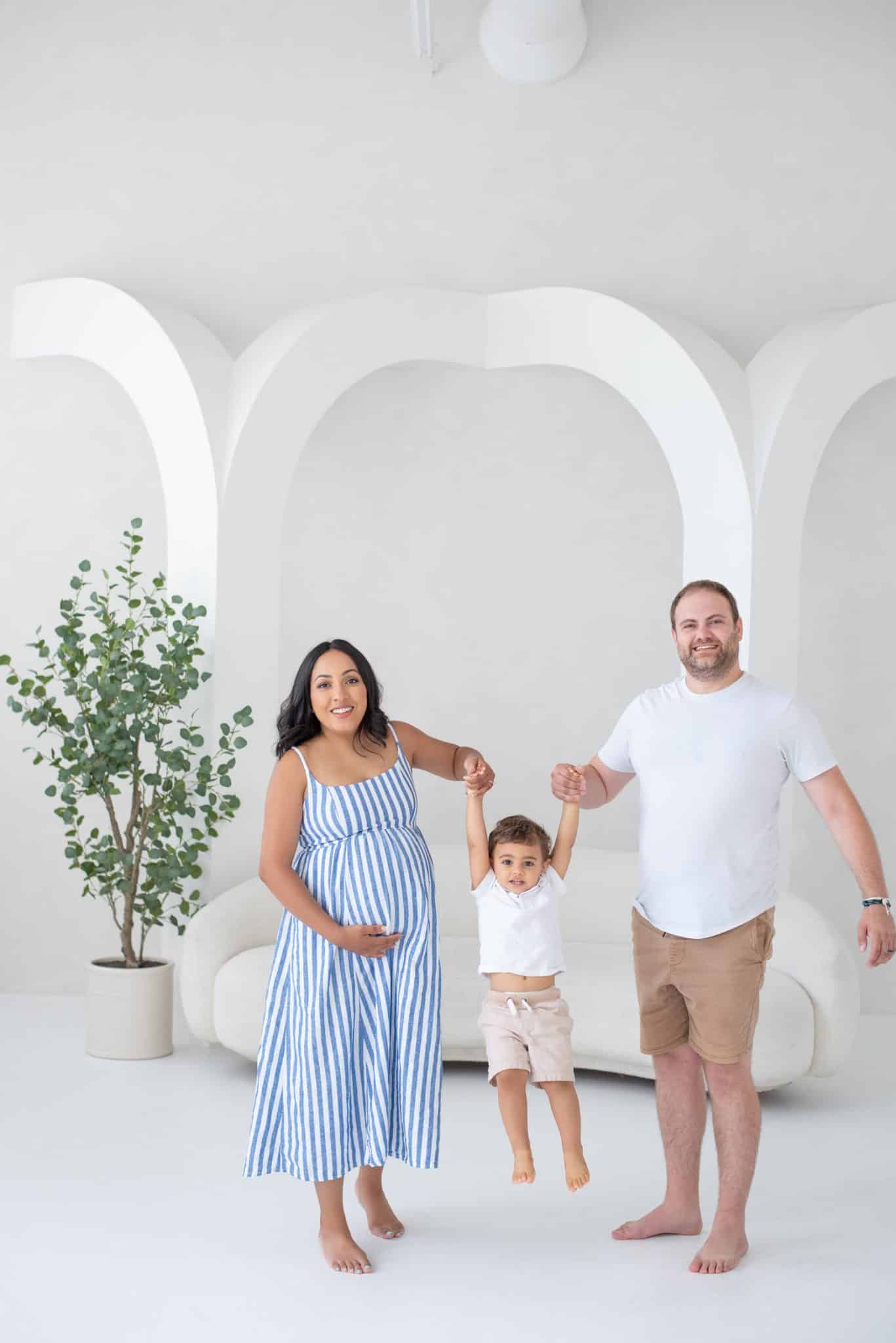 An expectant family posing together in a modern, minimalist studio setting for a professional maternity photo session Mississauga.