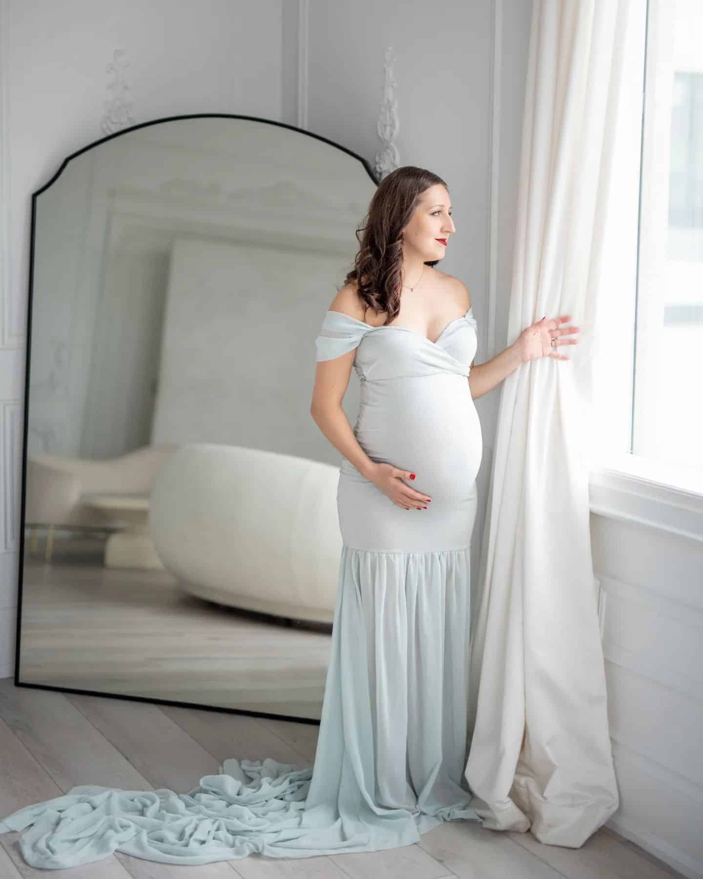 Elegant indoor maternity session in Toronto featuring mom-to-be in a flowing gown by the window