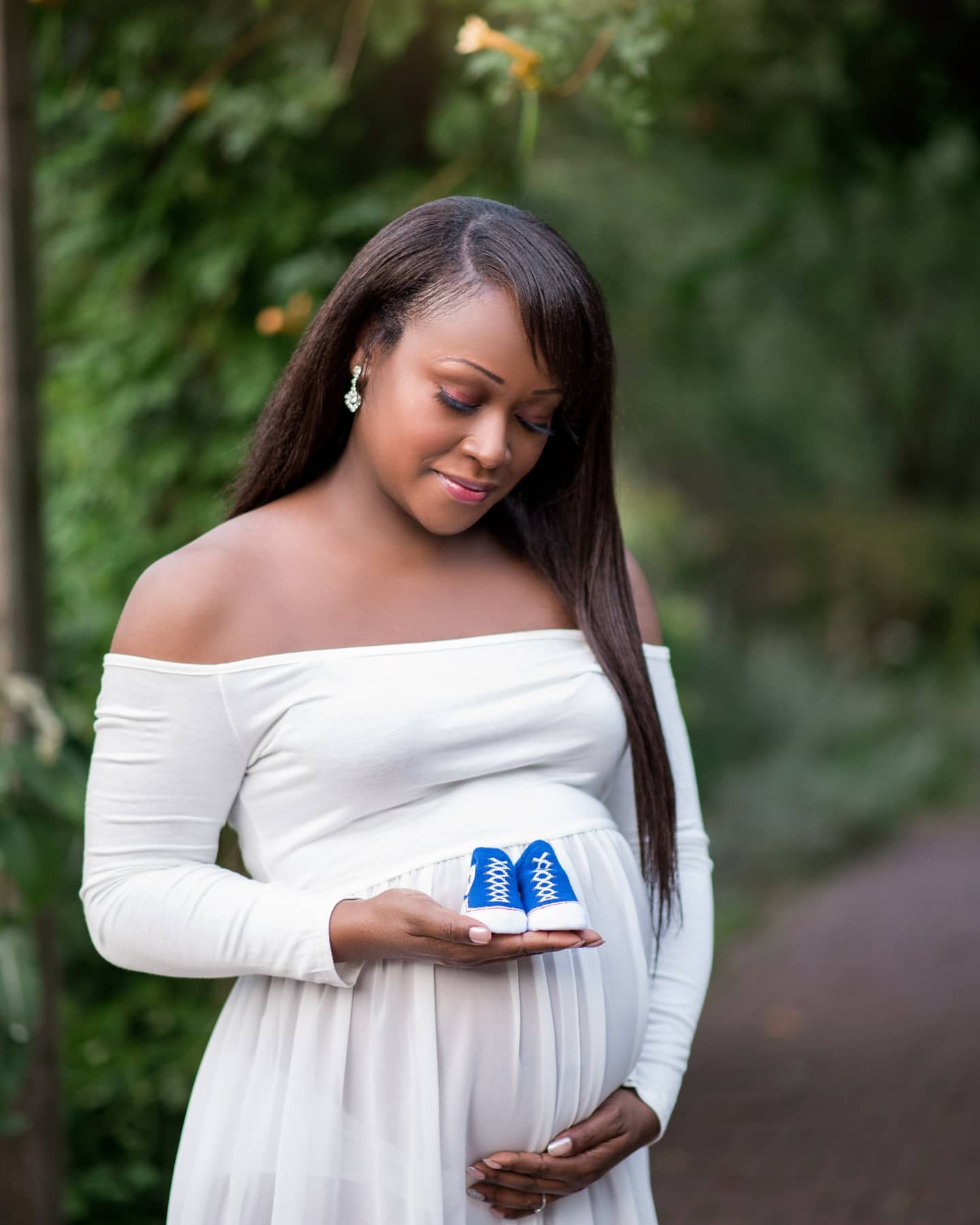 Outdoor pregnancy photoshoot Toronto with expecting mother holding baby shoes in a natural park setting
