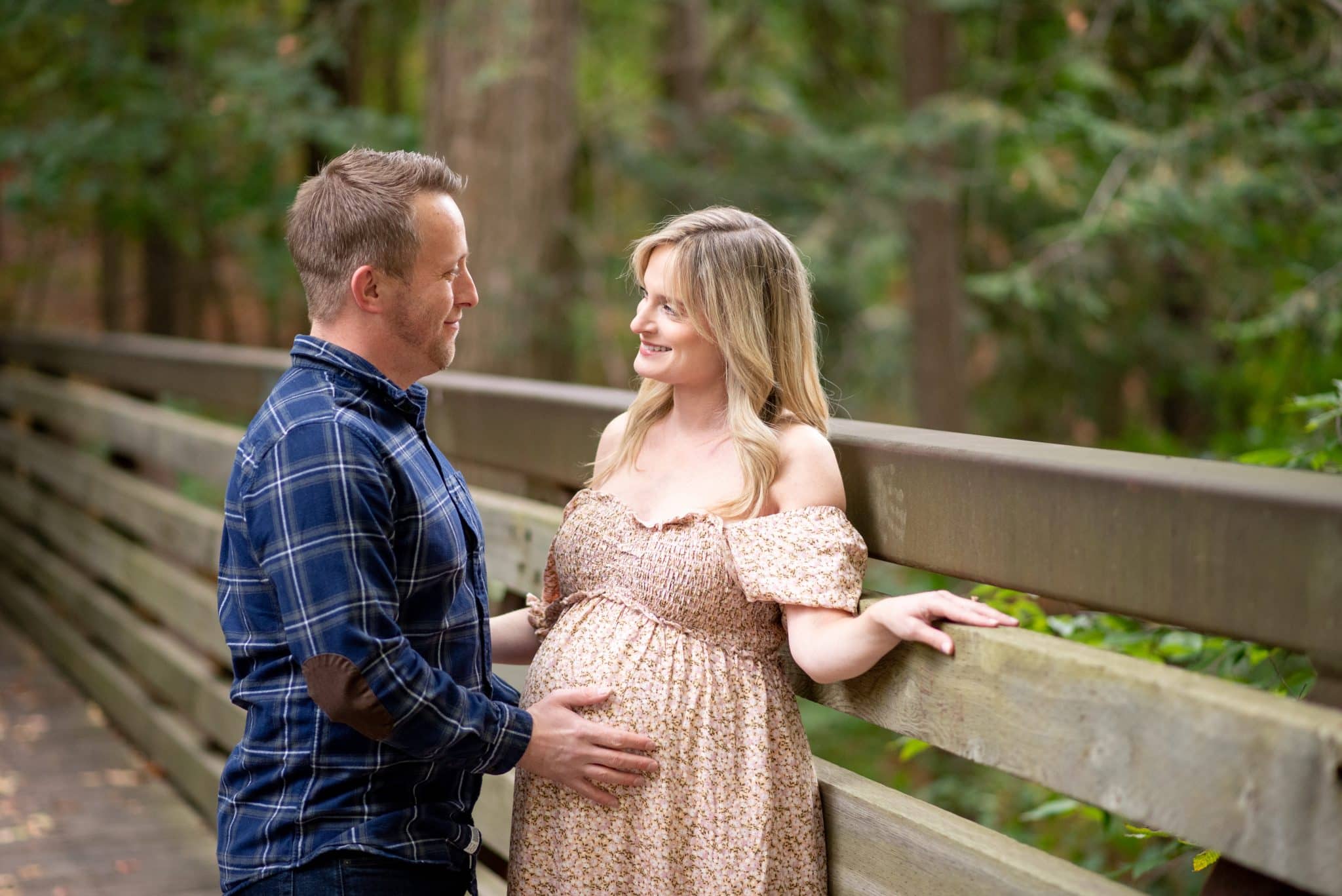 A couple sharing a close moment on a rustic wooden bridge in a forest, perfect for a natural maternity photo session in the GTA.