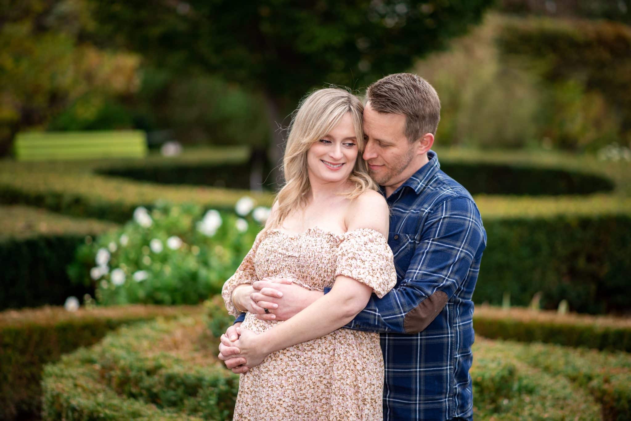 An expectant couple embracing in a beautifully manicured garden during their professional maternity photo session in Toronto.