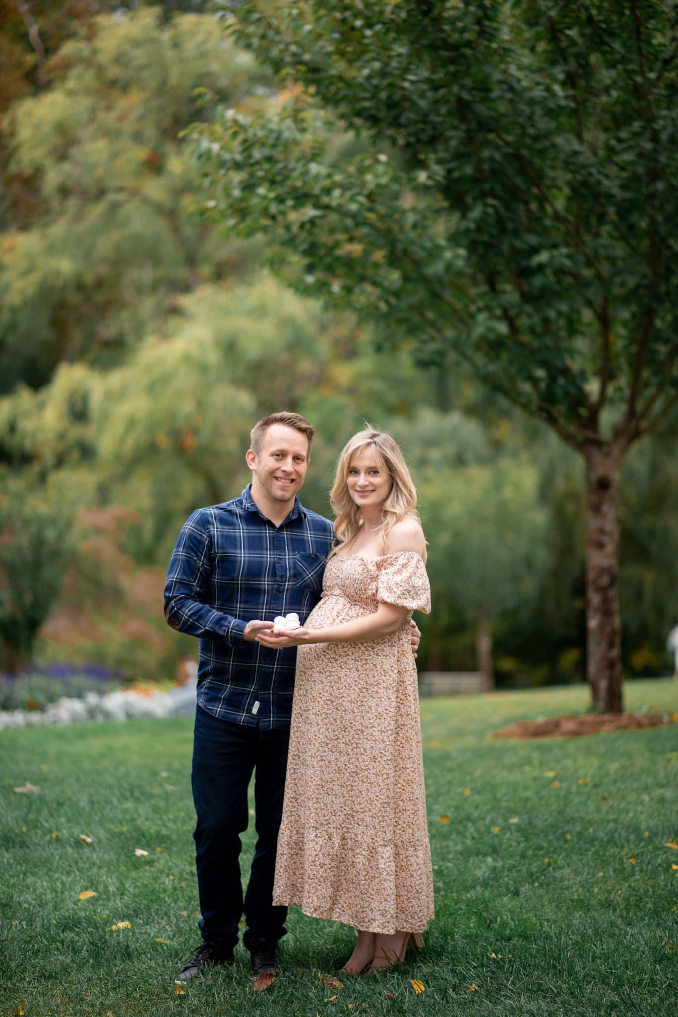 An expectant couple posing together in a lush, green park setting during their outdoor pregnancy photoshoot Brampton.
