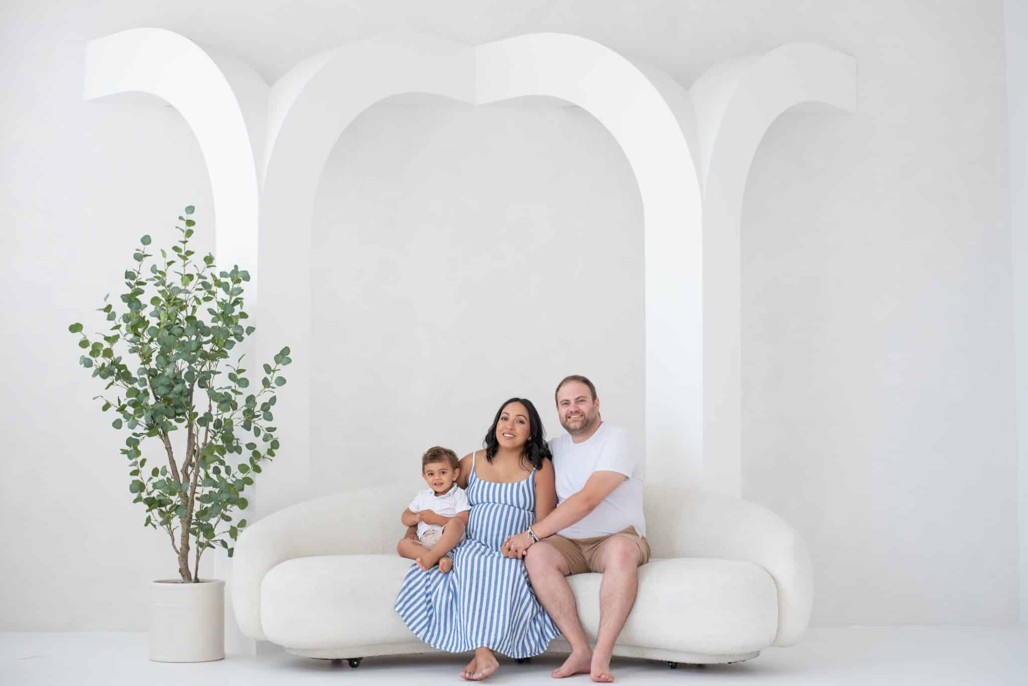 A beautiful family portrait featuring an expectant couple and their young daughter in a bright, white studio during a maternity photo session in Toronto.