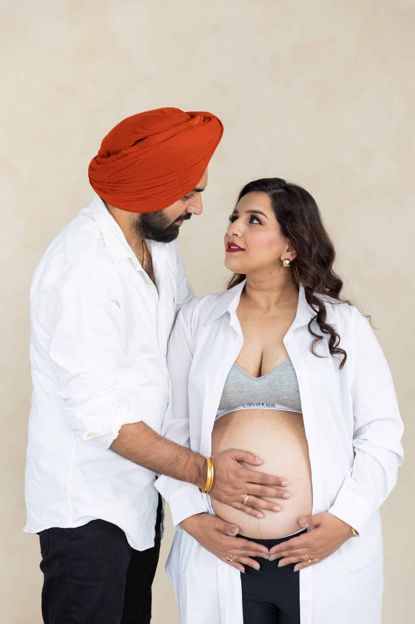 A man leaning in towards his pregnant partner's belly during a professional indoor maternity photo session in Toronto.