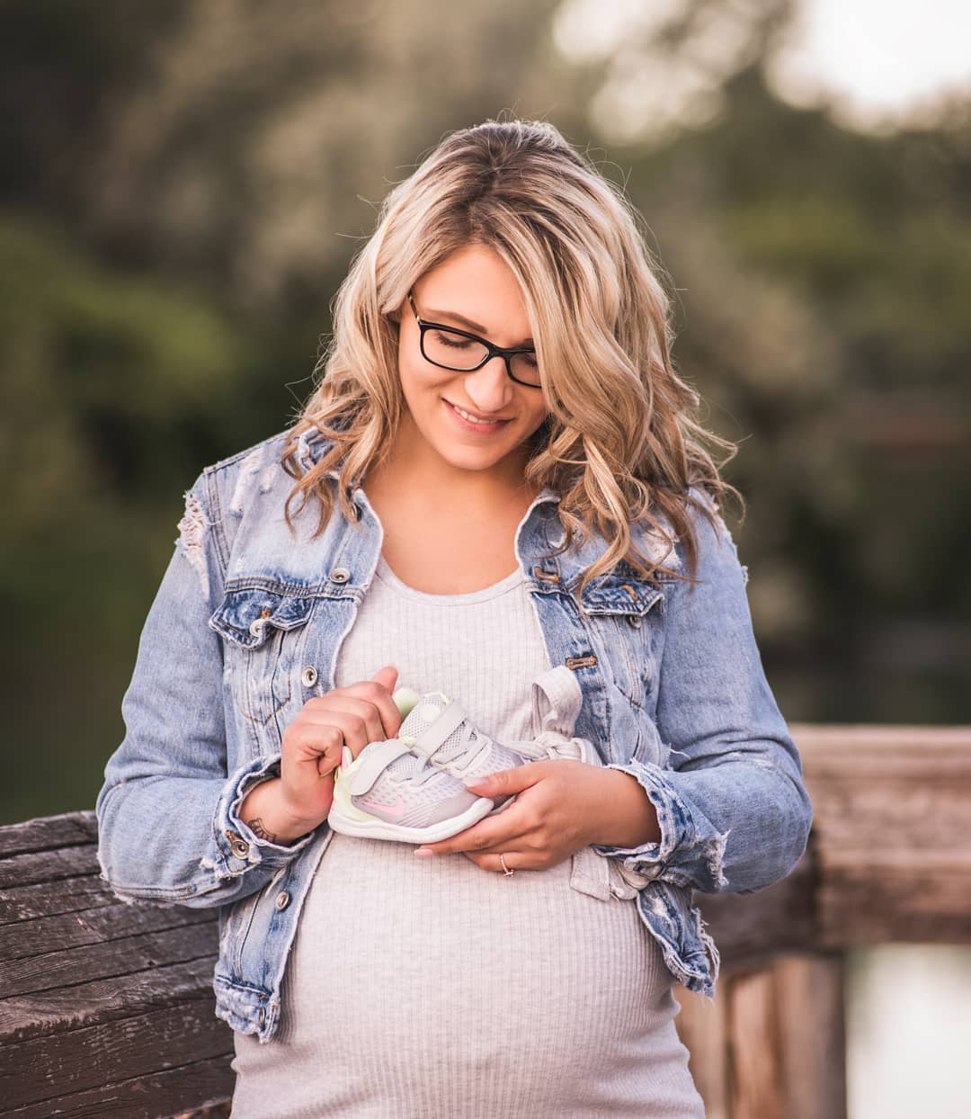 A pregnant woman in a denim jacket holding tiny white baby shoes over her belly during a professional maternity photo session in Toronto.