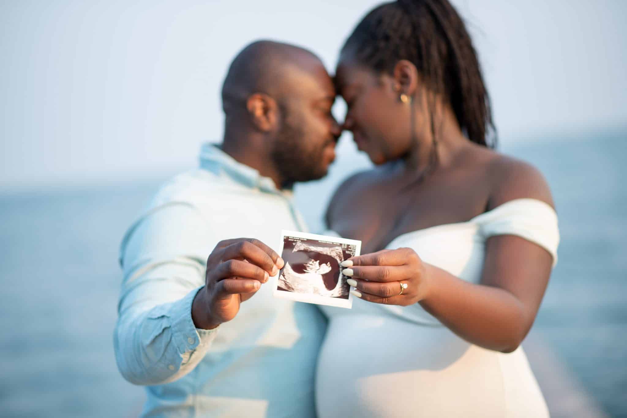A close-up of an expectant couple on a beach holding a sonogram photo during their romantic maternity photo session in Toronto.