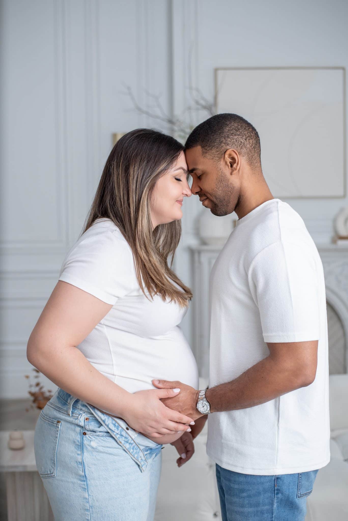 4 A close-up indoor portrait of an expectant couple in casual white attire sharing a loving gaze during a maternity photo session in the GTA.