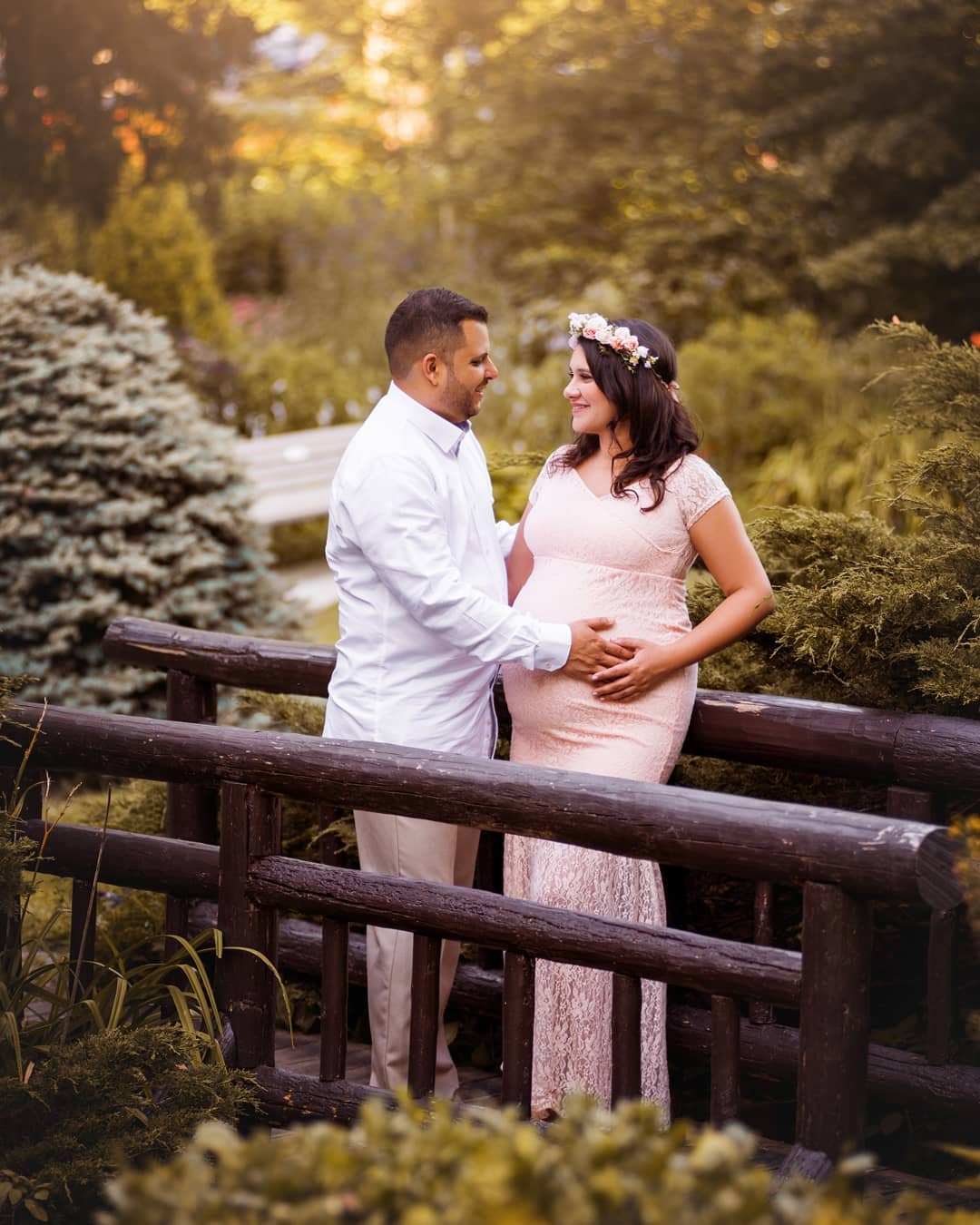 A couple sharing a tender moment on a wooden bridge in a beautiful garden setting for a maternity photo session in Oakville.