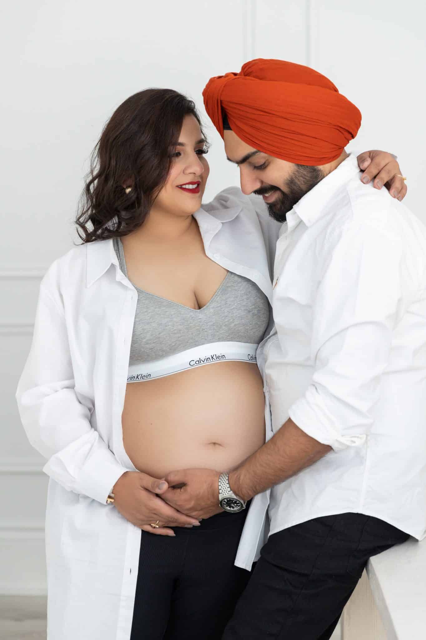 A vertical studio portrait of a pregnant woman and her partner in casual attire, capturing a loving connection for their maternity photo session Mississauga.