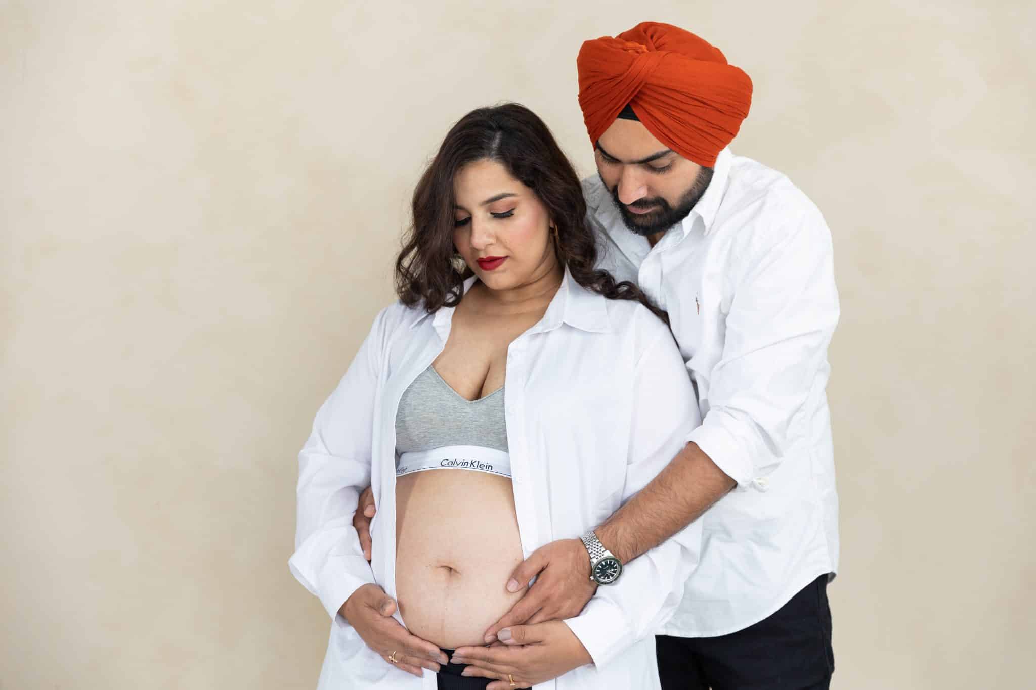 A horizontal studio portrait of an expectant couple in coordinated white shirts sharing a tender moment during a maternity photo session in Toronto.